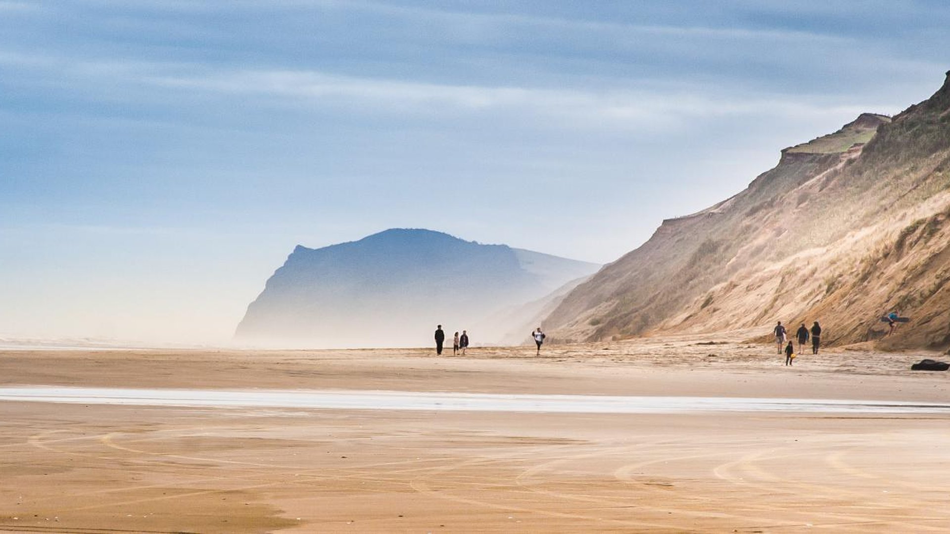 Walkers on the broad sands of Baylys Beach beneath Northland's coastal cliffs
