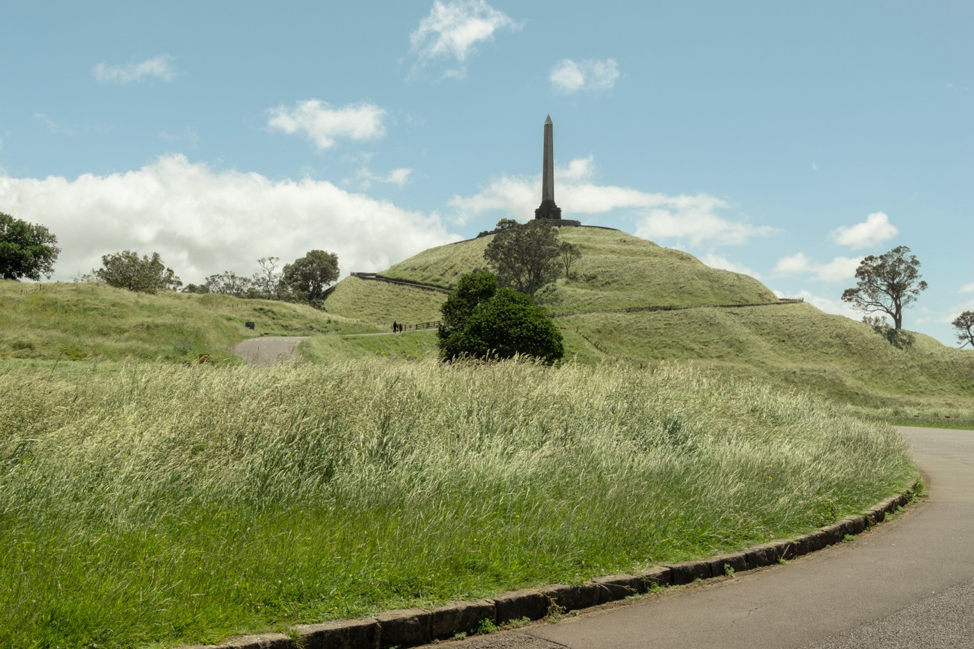 The winding road through grassy slopes toward the obelisk atop One Tree Hill in Auckland